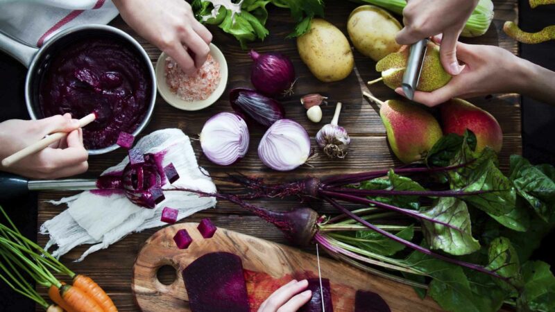 3 people cutting up vegetables on a chopping board