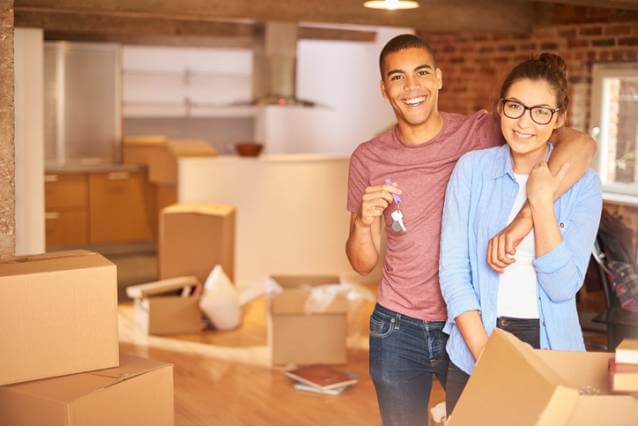 A couple holding the keys to their new home, surrounded by boxes