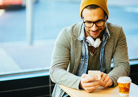 A man wearing a yellow hat and grey jacket, sitting in a cafe using a mobile phone