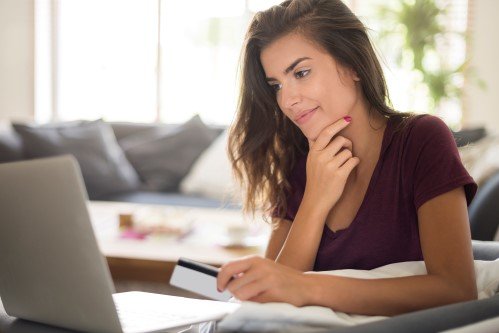 A woman sitting in front of a laptop, holding a bank card