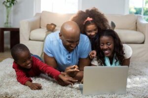 A family in their living room, smiling, looking at a laptop