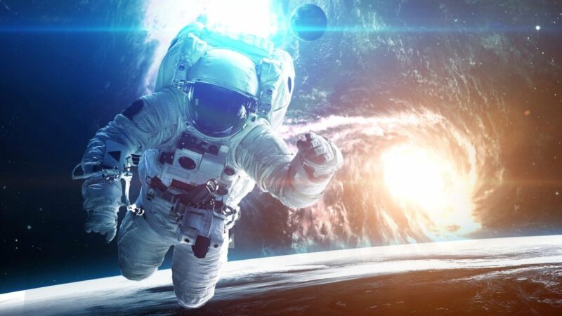 An astronaut, floating in space, behind him is a black hole