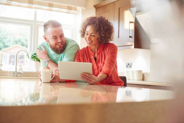 A couple, smiling looking at a tablet together in their kitchen