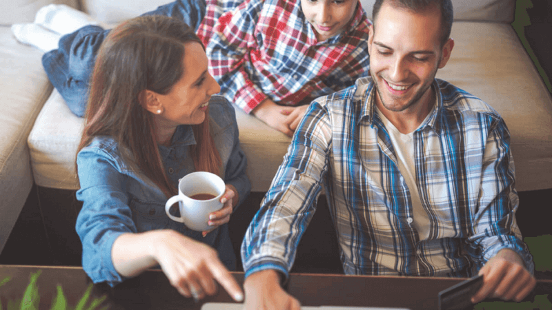 A family of three, laughing while pointing at a laptop