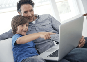 A father and son, laughing while pointing at a laptop