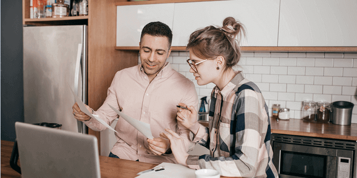 A couple, having a discussion while looking at a laptop and paper documents