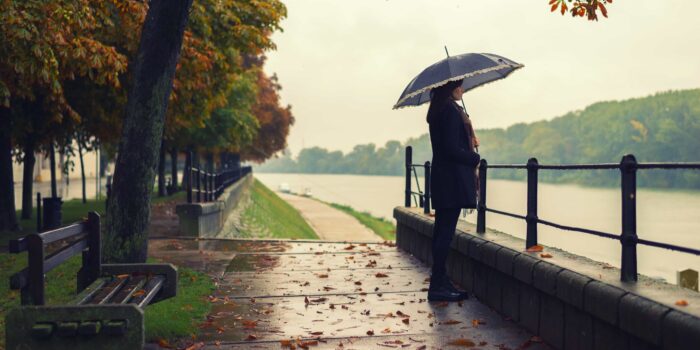 A woman standing in the rain while holding an umbrella, looking over a river