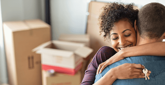 A young couple, hugging eachother and holding the keys to their new home