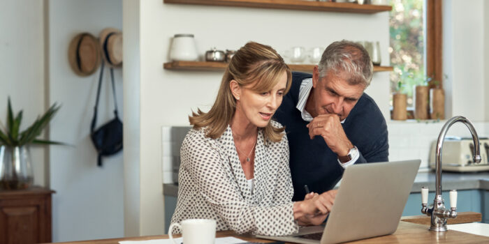 a middle-aged couple sitting in front of a laptop making a decision